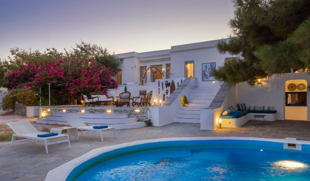 Villa Ari private pool in Sifnos — illuminated swimming pool at twilight with bougainvillea, sun loungers, and whitewashed Cycladic villa facade