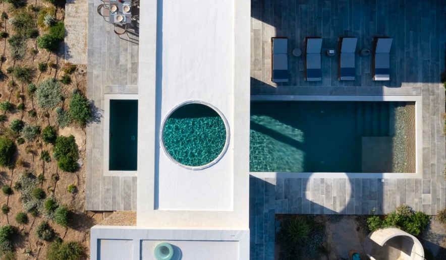 Villa Louise Sifnos aerial view — modern architecture with round plunge pool, rectangular infinity pool, sun loungers, and Mediterranean landscaping above Vathy bay